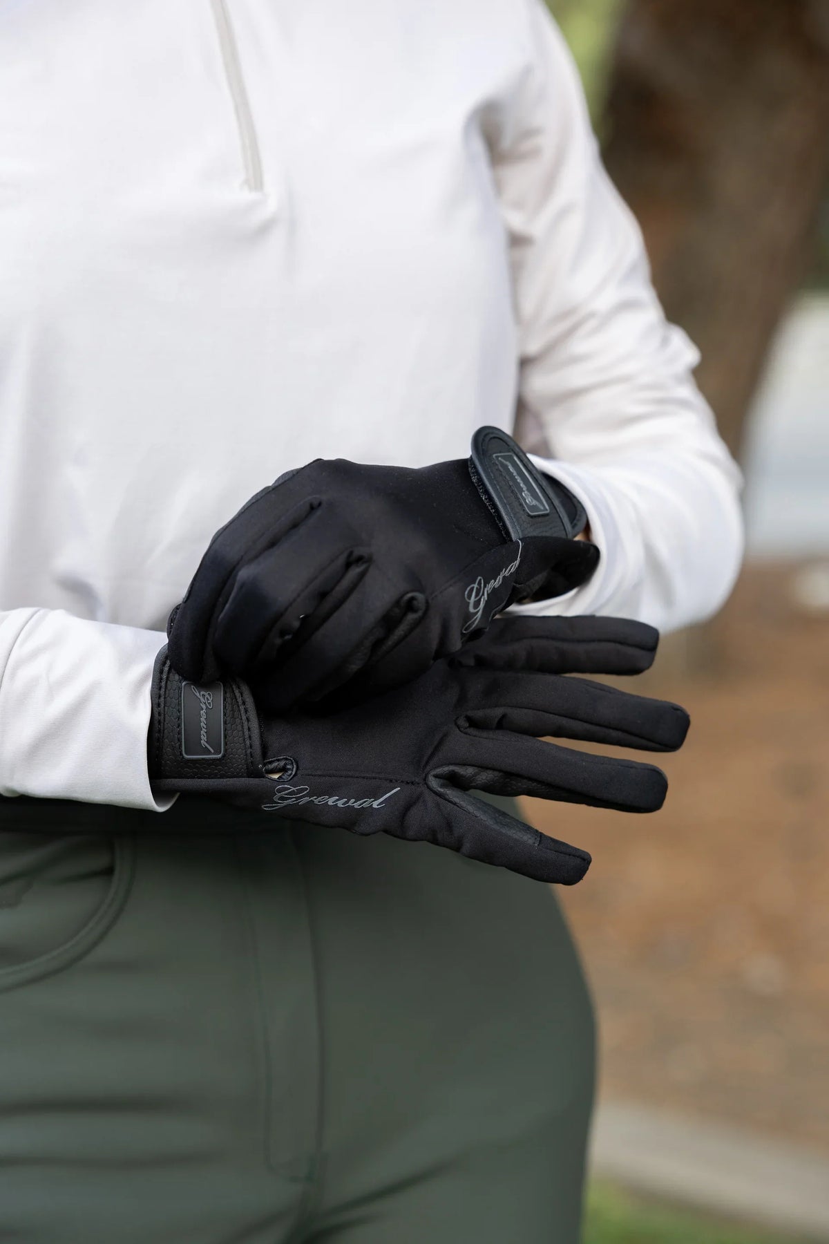 Rider in a white quarter-zip and green breeches wearing black riding gloves