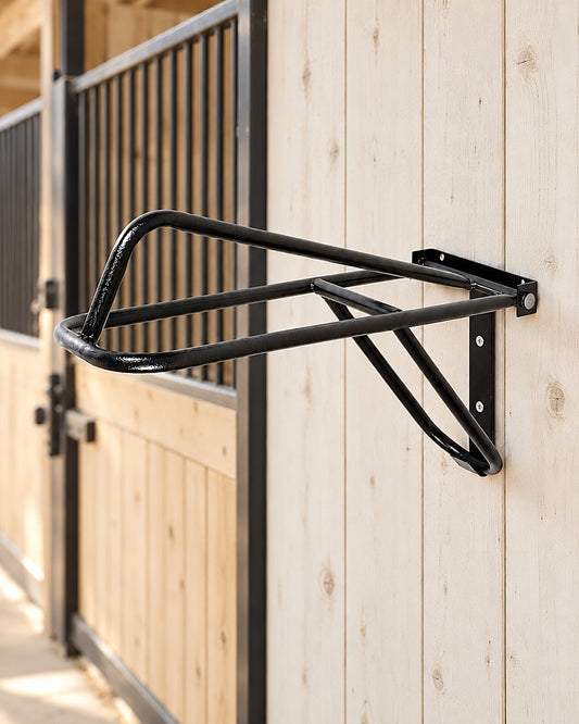 HDR fold down saddle rack in black, screwed to a whitewashed barn wall beside a stall