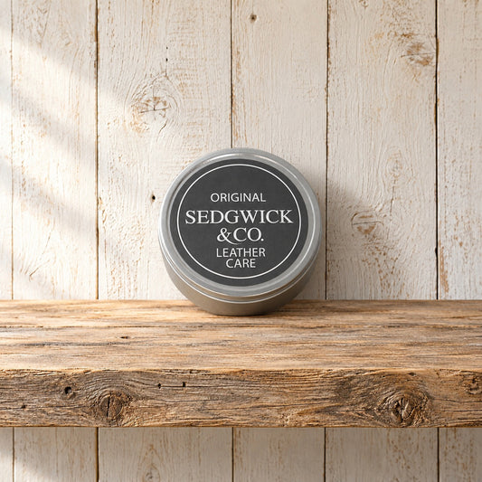 Sedgwick and Co leather care tin leaning against the wall on a rough wood shelf
